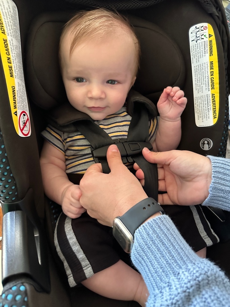 student clipping the chest strap of a baby in a car seat.
